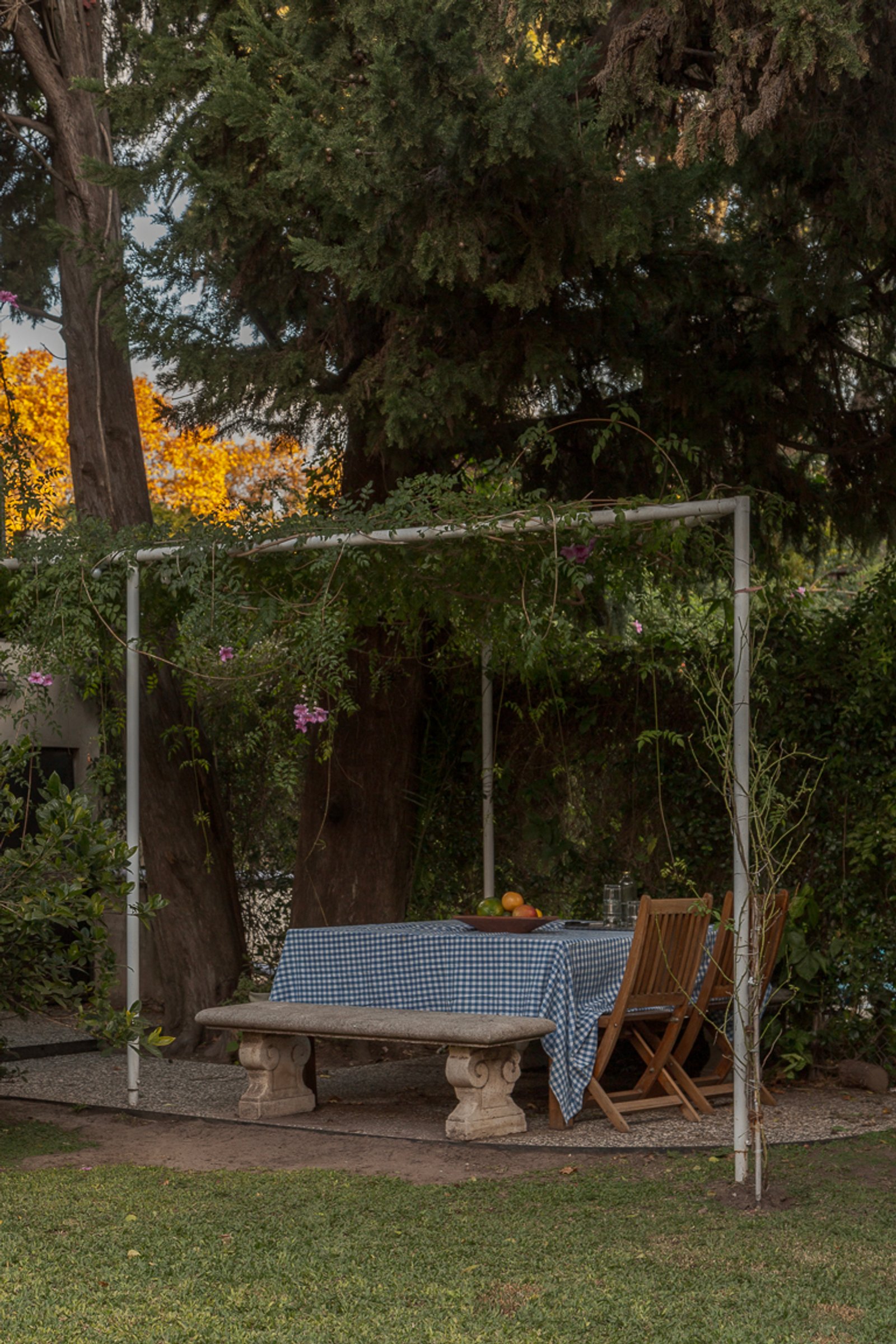 Patio exterior con pérgola, banco de piedra y mesa a cuadros — proyecto Jardines Catamarca, por Estudio YME, en B1636 Olivos